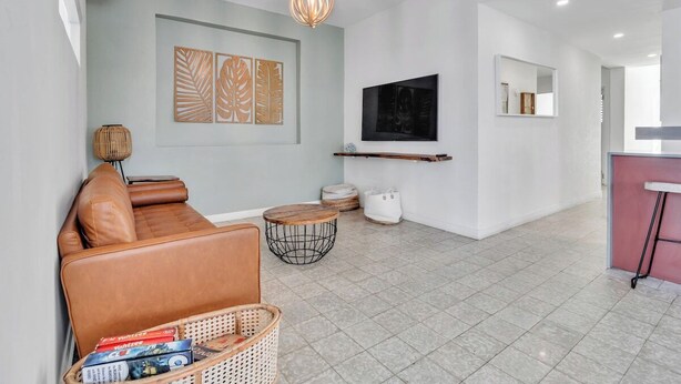A modern living room with a leather sofa, a TV, and a wall-mounted shelf. - Villa Coco: Private Pool | 5 Min Walk to Beach (San Juan)