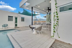 A modern outdoor pool area with a table and chairs, a covered seating area, and a view of the sky. - Villa Coco: Private Pool | 5 Min Walk to Beach (San Juan)