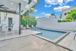 Ett modernt utomhusområde med pool, solstolar och en bar.