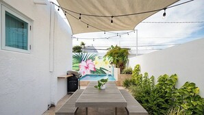 A patio with a wooden table and benches, surrounded by plants and a mural.