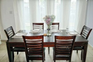 Een eettafel met vier stoelen, een vaas met bloemen en een glas water.