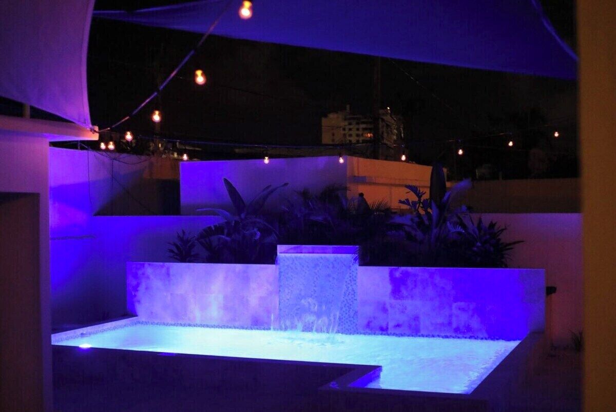 An outdoor water feature with a tiered design, illuminated by blue lighting, surrounded by plants.