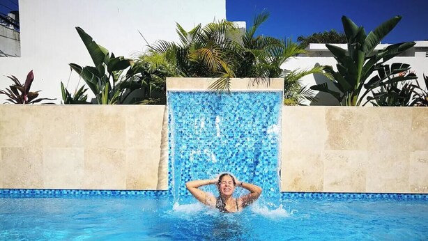 A person in a swimming pool with a waterfall feature.