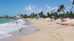 Een strand met palmbomen, parasols en mensen.
