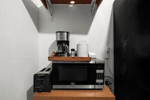 A kitchen area with a microwave, toaster, coffee maker, and a small cabinet.