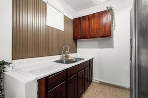 Una cocina con encimera de mármol, armarios de madera y pileta de acero inoxidable, además de un refrigerador.