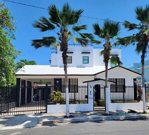 A modern two-story building with a white facade, black-framed windows, and a gated entrance.