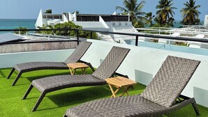 Des fauteuils de jardin confortables, placés sur une pelouse artificielle, offrent une vue sur la mer et les bâtiments qui se dressent à l’arrière-plan.
