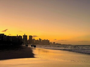 A beach with a city skyline in the background during sunset.