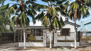 A residential property with a white exterior, a gated entrance, and palm trees. - Ocean View Rooftop | Rattan Retreat – 1BR (San Juan)