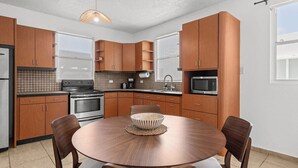 A modern kitchen with wooden cabinets, a round dining table, and a hanging light fixture. - Ocean View Rooftop | Bamboo Breeze – 2BR (San Juan)