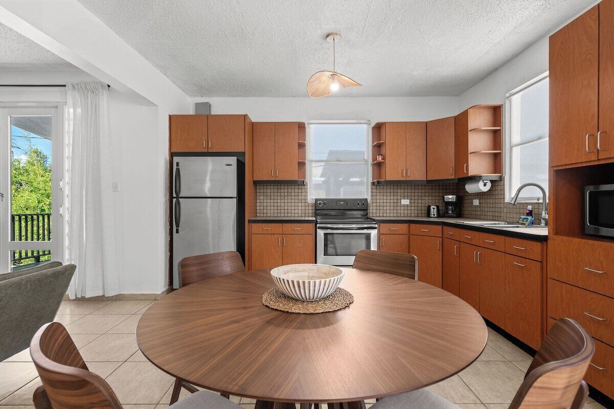 A modern kitchen with wooden cabinets, a stainless steel refrigerator, and a round dining table with chairs.