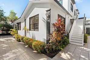 A white building with a staircase and a garden with various plants.