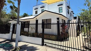 A modern two-story house with a white exterior, black gates, and a yellow awning. - Ocean View Rooftop | Bamboo Breeze – 2BR (San Juan)