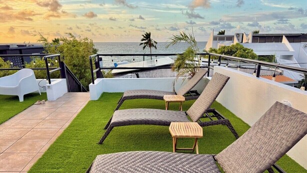A rooftop terrace with outdoor lounge chairs, a small table, and a view of the ocean. - Ocean View Rooftop | Bamboo Breeze – 2BR (San Juan)