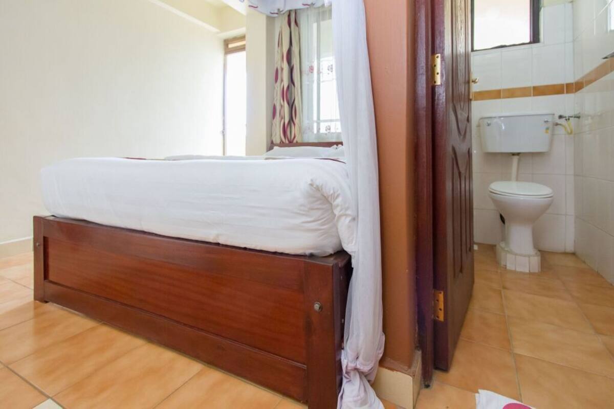 Une chambre à coucher avec un lit en bois, un matelas blanc, une porte en bois et des toilettes blanches dans une salle de bain.