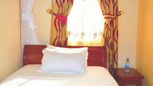 Quarto de hotel com cama, mesa de cabeceira e cortinas.