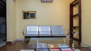 Uma área de espera com três cadeiras de metal e uma mesa de vidro com revistas.
