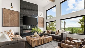 Un salon moderne doté d’une cheminée, de grandes fenêtres et offrant une vue sur une tour distante.