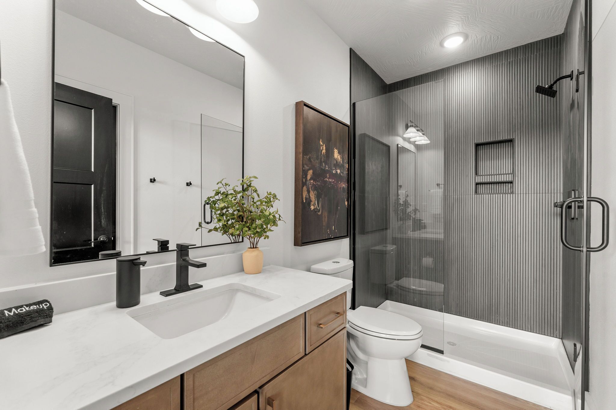 A modern bathroom with a large mirror, a sink, a toilet, and a shower area.