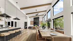 Une cuisine moderne dotée d’un grand îlot central, de tabourets de bar en bois et d’un coin repas avec une longue table et des chaises.