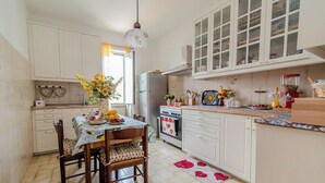 A kitchen with white cabinets, a dining table with chairs, a refrigerator, an oven, and a window with curtains. - Casa Marino (Ciampino)