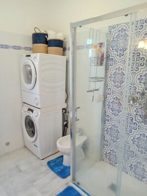 A compact bathroom with a washing machine, a toilet, and a shower enclosure.
