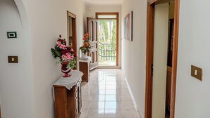 A hallway with a wooden console table, a vase of flowers, and a door leading to a balcony with a view of trees. - Casa Marino (Ciampino)