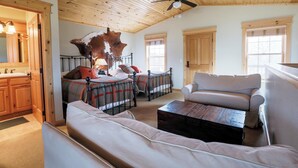 A spacious living area with a high ceiling, a bed with a headboard, a sofa, a coffee table, and a large window. - Cabin 3 at the Almo Inn, Close to City of Rocks National Park and Castle Rock (Almo)