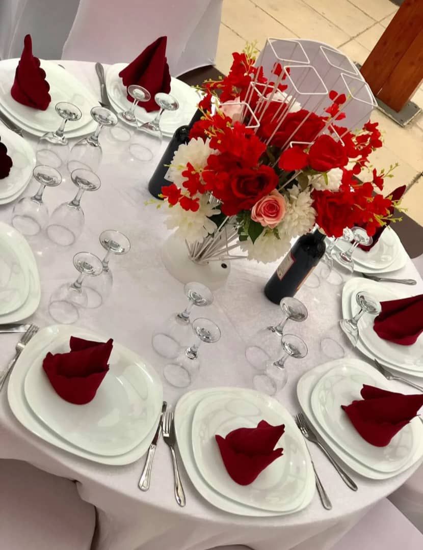 A table set for a formal event with white plates, red napkins, and a centerpiece of red and white flowers.