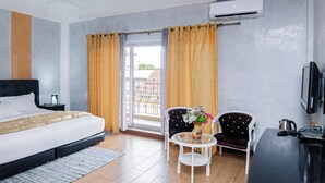 Habitación de hotel con cama, una mesita con un florero, dos sillas, un televisor y un aire acondicionado.