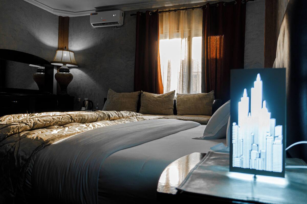 A hotel room with a bed, a nightstand, a lamp, and a cityscape artwork on the wall.