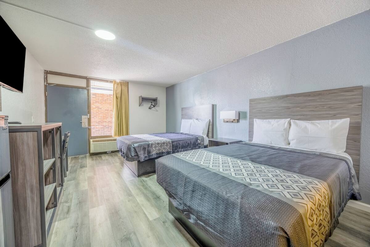 Ein Hotelzimmer mit zwei Betten, einem Schreibtisch und einem Fenster mit Vorhängen.