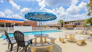 A poolside area with a blue umbrella, outdoor seating, and a building in the background. - Oyo Hotel Bartow (Bartow)