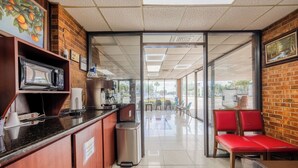 A clean, modern interior with a kitchen area, a seating area with red chairs, and a view through a glass door to the outside. - Oyo Hotel Bartow (Bartow)