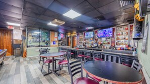 A bar area with multiple tables and chairs, a counter with various bottles, and a television screen. - Oyo Hotel Bartow (Bartow)