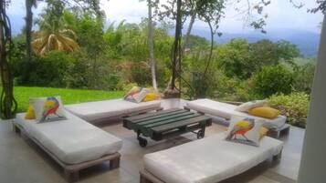 Relax in a serene outdoor lounge surrounded by lush greenery and a mountainous view.