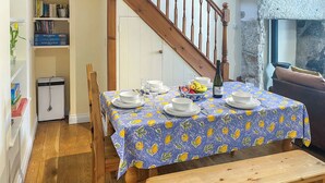 Un coin repas avec une table dressée pour quatre personnes, un banc, une bibliothèque et un escalier.