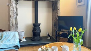Un salon chaleureux avec une cheminée en pierre, un téléviseur et une table où sont disposés des pâtisseries et des tasses à café.