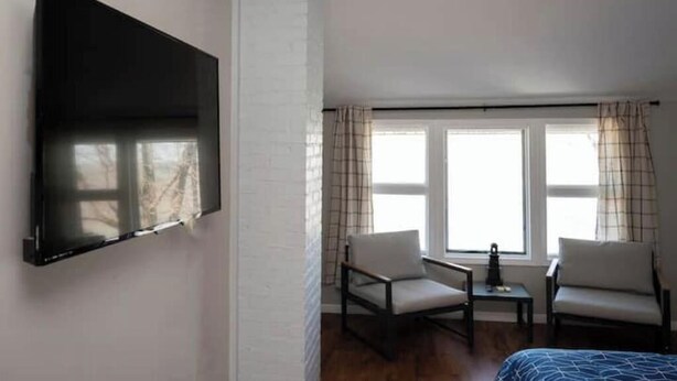 A hotel room with a flat-screen TV mounted on the wall, two chairs, a small table, and a bed. - Spacious Vermilion House on the Lake (Vermilion)