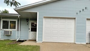 A two-story house with a garage, a front door, and an air conditioning unit.