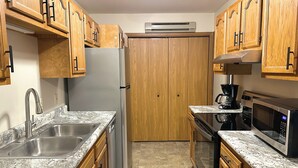 A kitchen with granite countertops, wooden cabinets, a stainless steel refrigerator, a coffee maker, and a microwave.