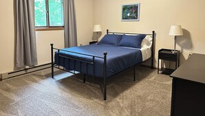 A bedroom with a bed, two bedside tables with lamps, a window with curtains, and a painting on the wall.
