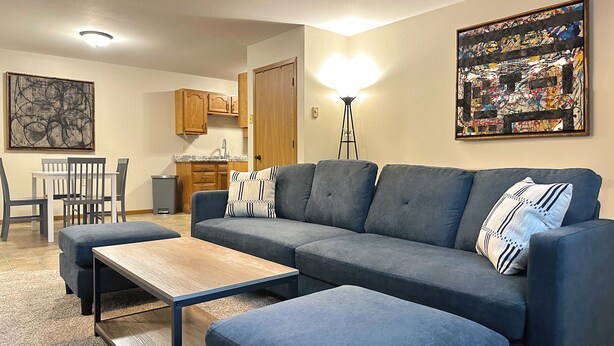 A modern living room with a sectional sofa, a wooden coffee table, and a dining area with a white table and chairs.