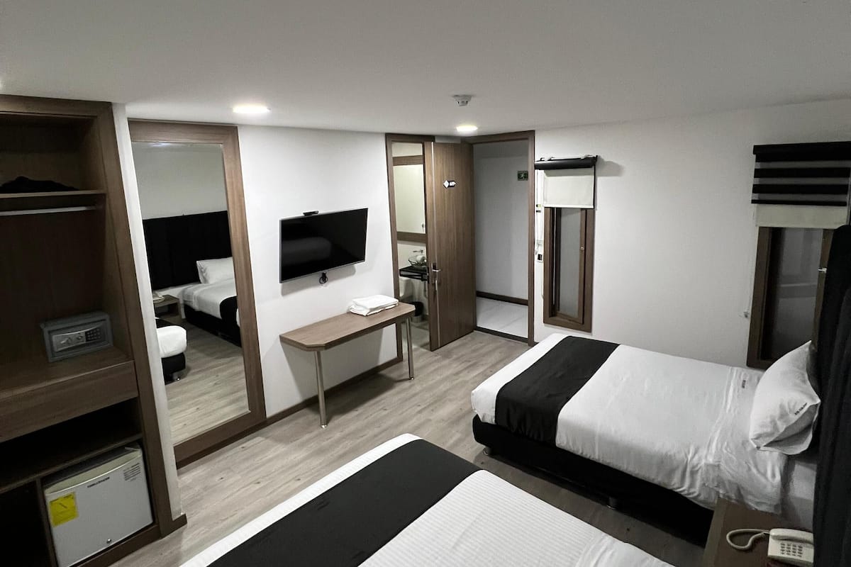 Ein Hotelzimmer mit zwei Betten, einem Schreibtisch, einem Fernseher und einem Kleiderschrank.