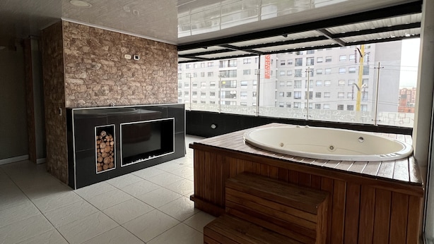 Een moderne badkamer met een stenen muur, een houten wastafelmeubel, een groot bad en een uitzicht op een stadsgezicht door een groot raam.