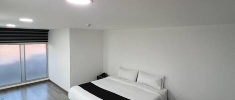 A modern bedroom with a large bed, a bedside table, a black sofa, and a large window with a view.