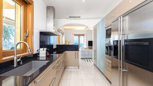 A modern kitchen with stainless steel appliances, a black countertop, and a view of the living area. - Magnificent sea view villa - DG (Cap-d'Ail)