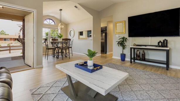 Un amplio salón con mesa de comedor, un televisor de pantalla plana en la pared y una cocina moderna al fondo.