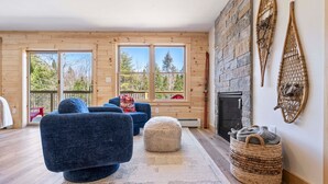 A cozy living room with a fireplace, wooden walls, and large windows. - Pointers Den-Fireplace, Arcade, 2 Primary Suites (Bethel)